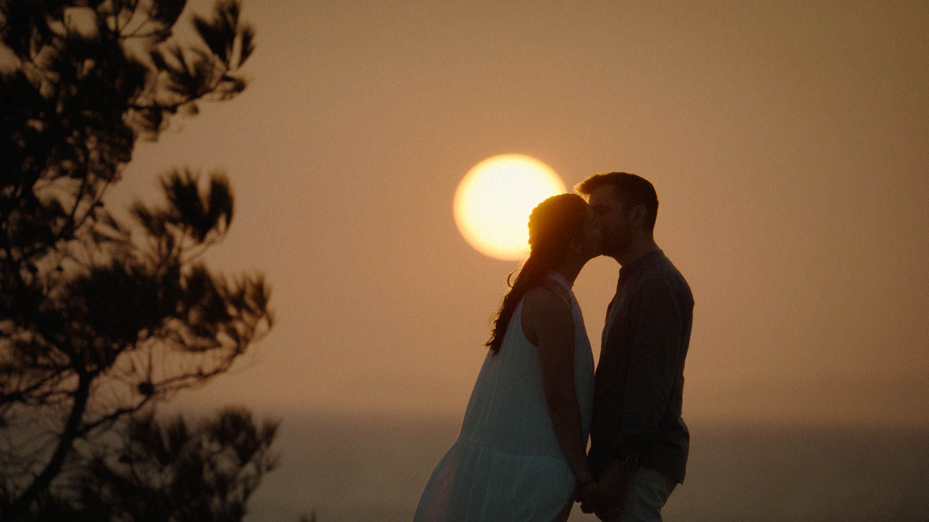 Silhouetted couple in wedding attire share an intimate moment as the sun sets behind them creating a romantic golden glow.