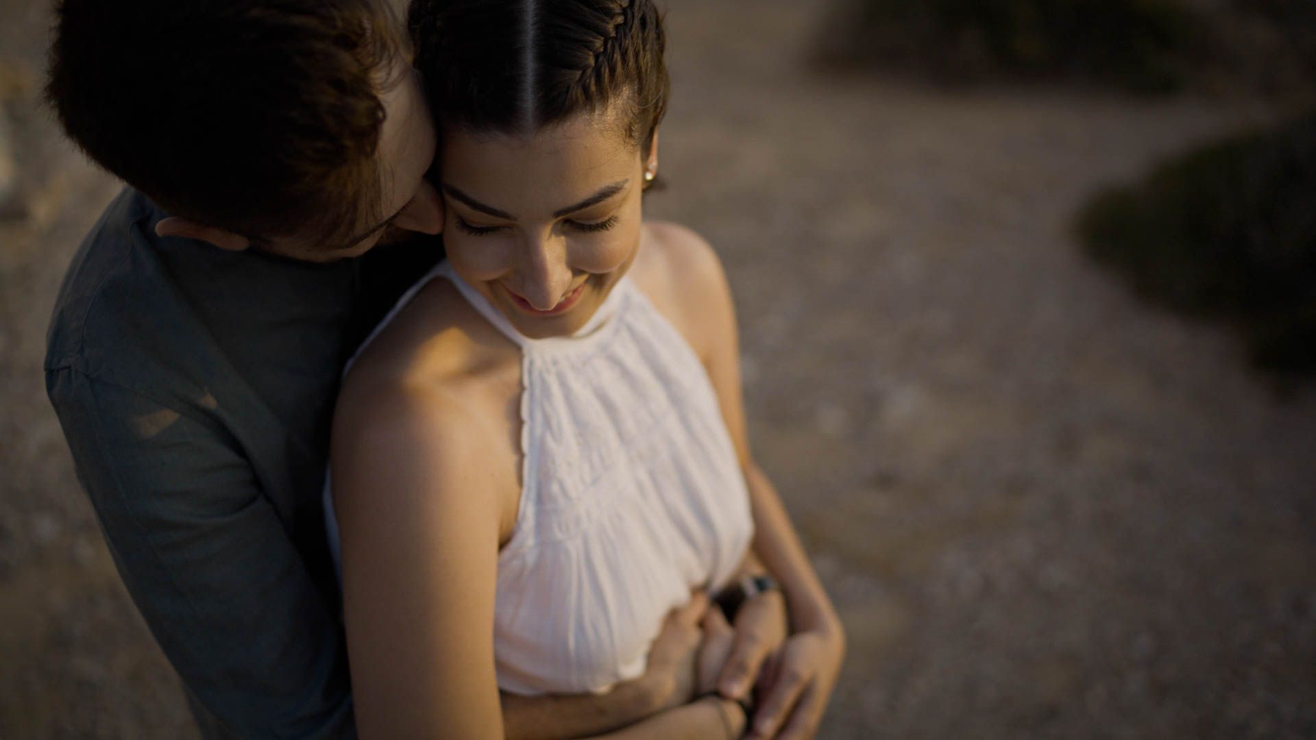 A tender moment between a couple embracing at sunset, with soft lighting highlighting their intimate connection.