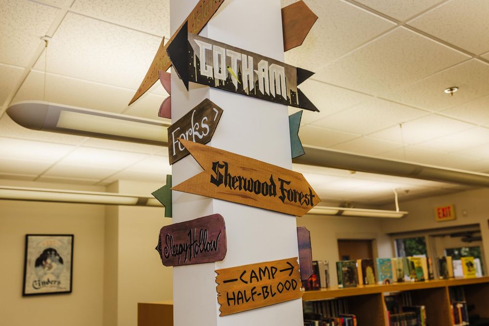 Handmade wooden directional sign post with multiple arrows pointing to fictional locations like Lothlórien and Sherwood Forest.