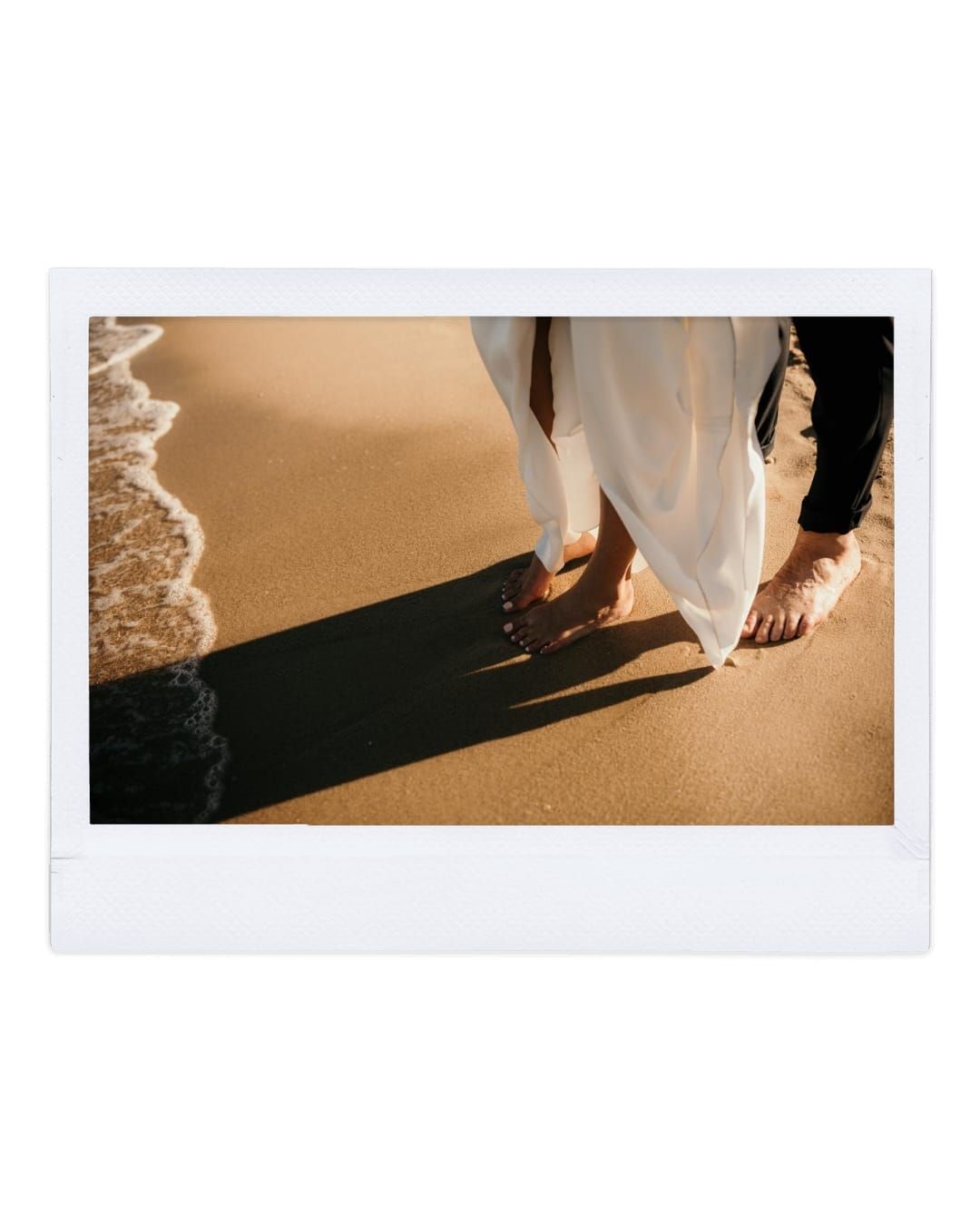 Close-up of feet walking on a sandy beach with ocean wave and shadow cast on golden sand.