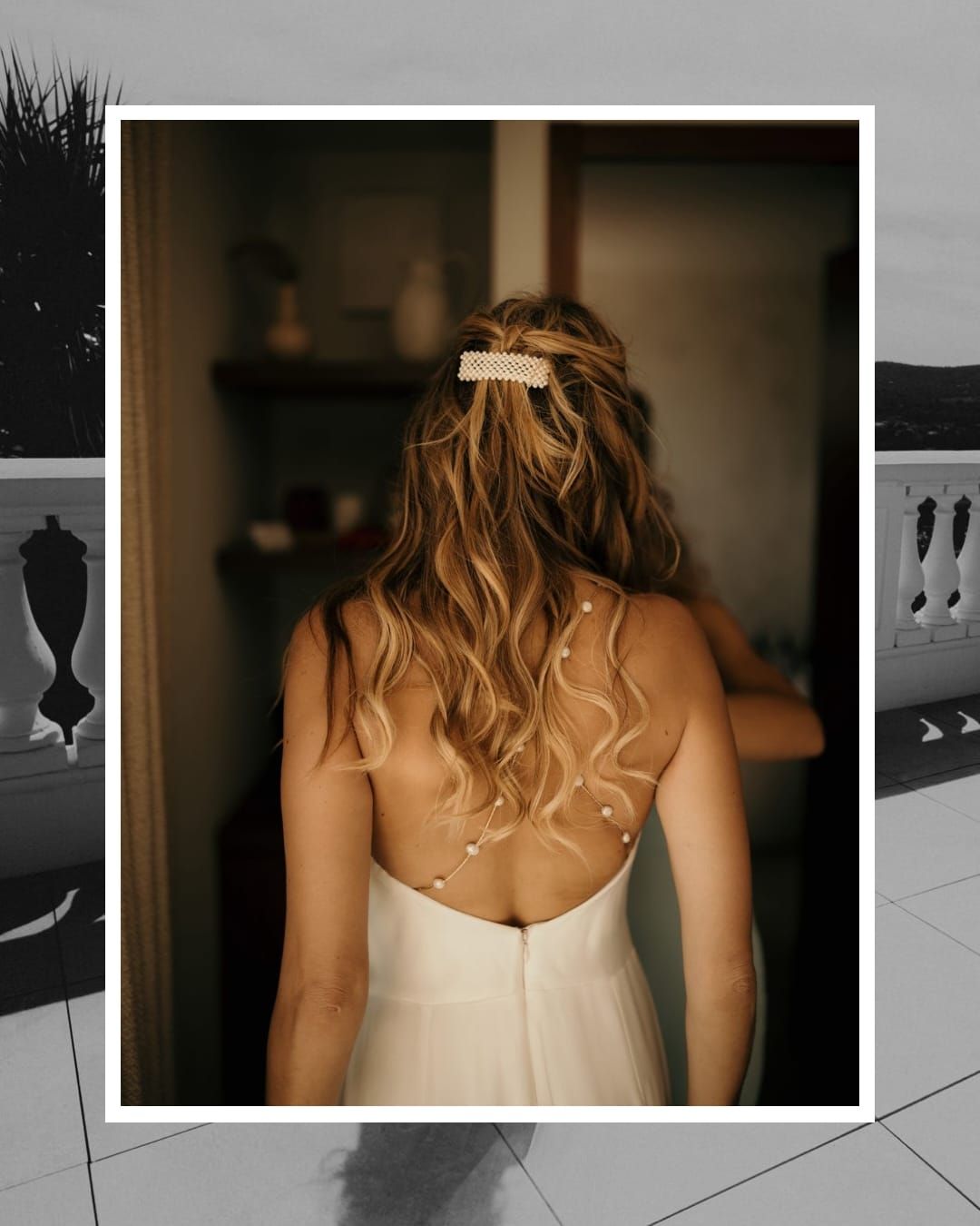 Back view of a bride in white dress with wavy blonde hair adorned with a delicate hair accessory in a dimly lit room.