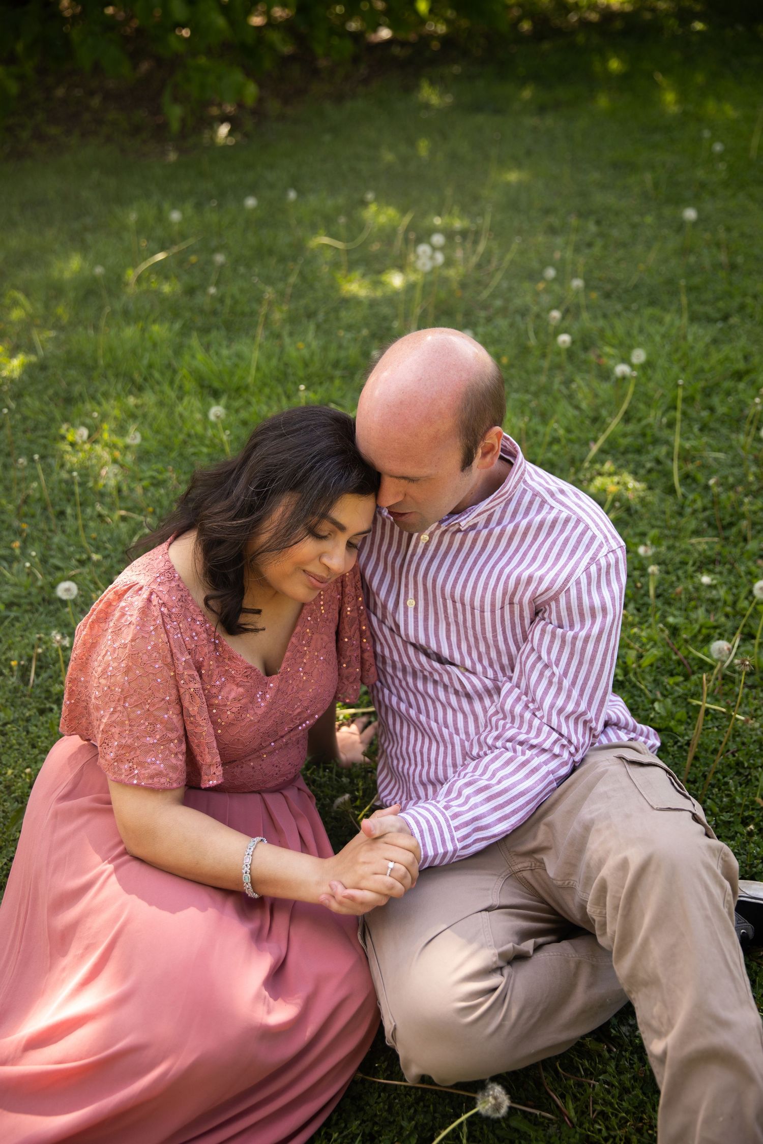 Couple sharing an intimate moment sitting together on green grass in a garden setting wearing pink and striped clothing.