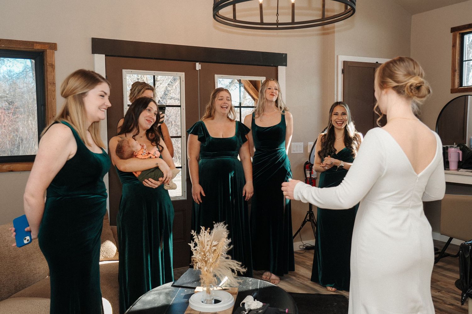 Bridesmaids in emerald velvet dresses gather with the bride in an elegant room during wedding preparations.