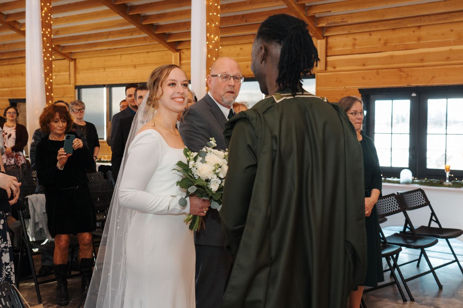 Wedding ceremony taking place inside rustic wooden venue with natural light streaming through windows.