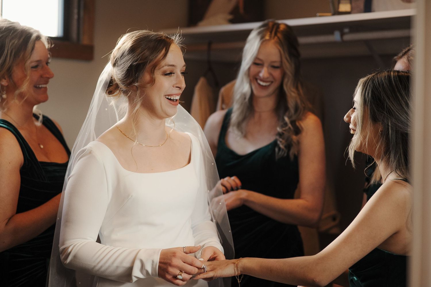 A bride in a long-sleeved white dress shares a joyful moment with her bridesmaids wearing black dresses.