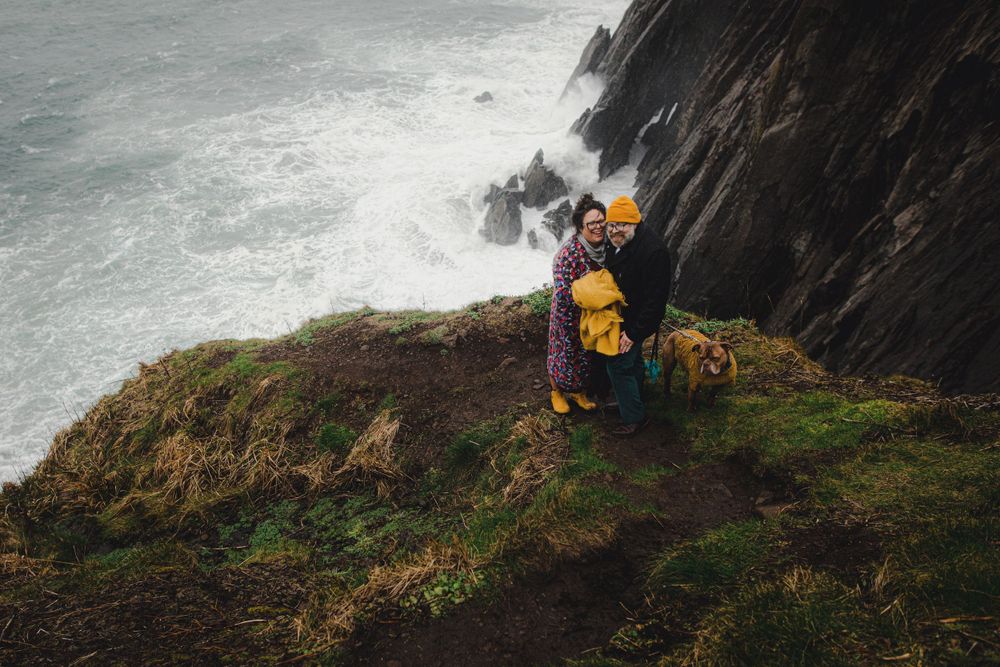 Figure in bright yellow against dramatic coastal cliffs and crashing ocean waves below.