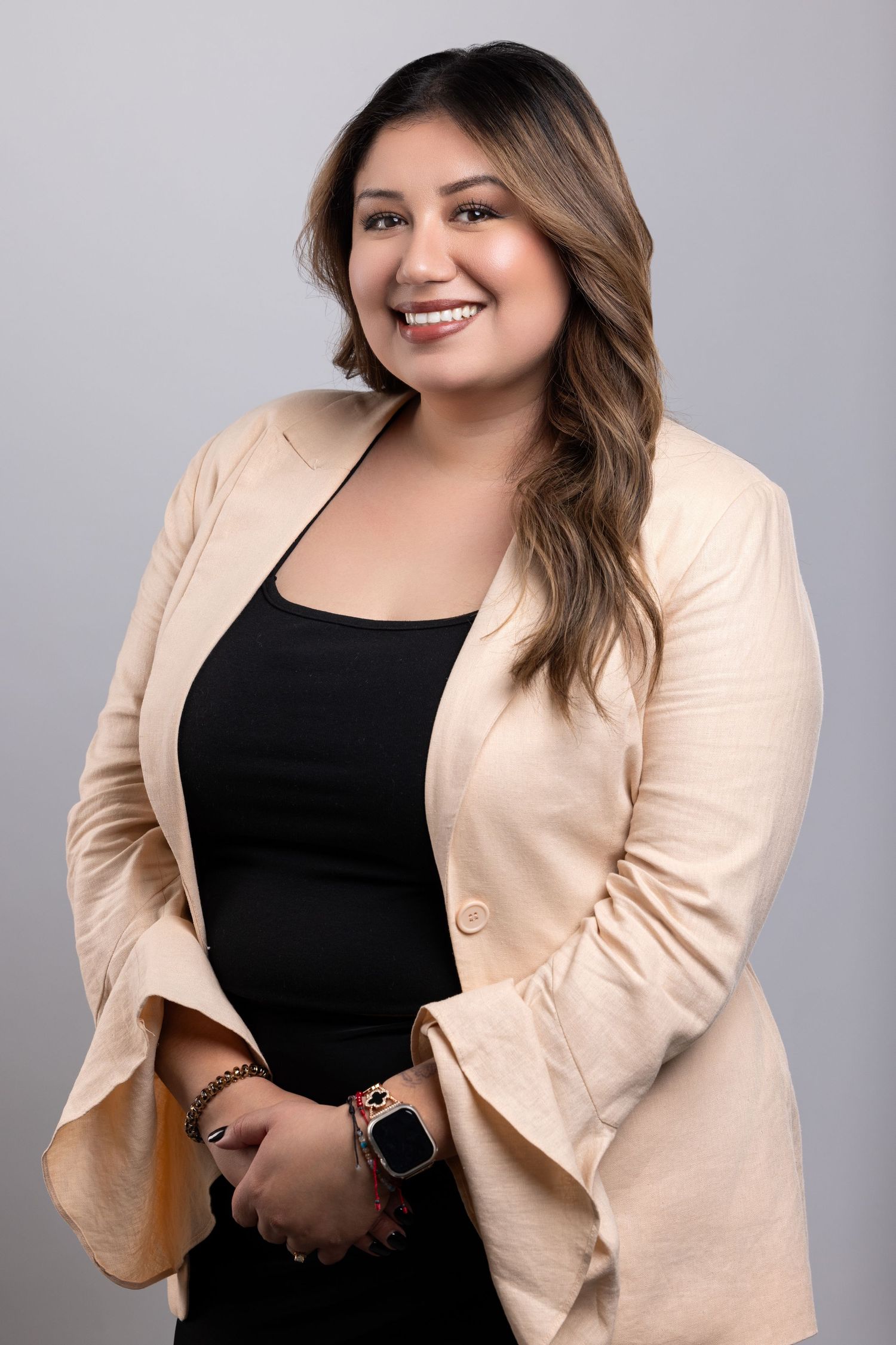 Professional portrait in beige blazer and black top against gray studio background.