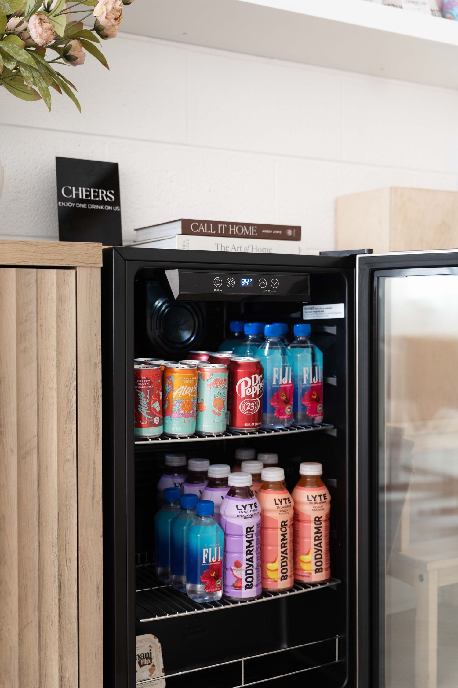 Black mini fridge stocked with colorful cans and bottles of beverages on shelves with books displayed on top.