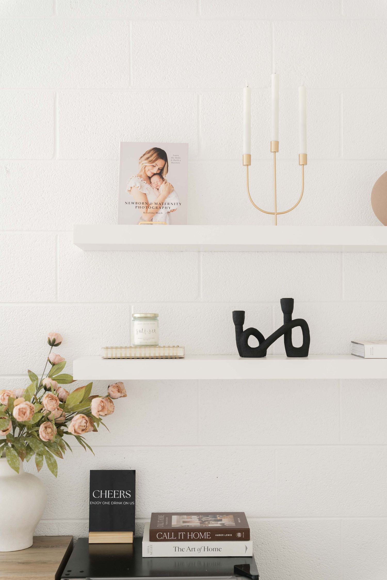 Modern white wall shelves styled with a gold candelabra, black abstract sculpture, fresh flowers and decorative books.