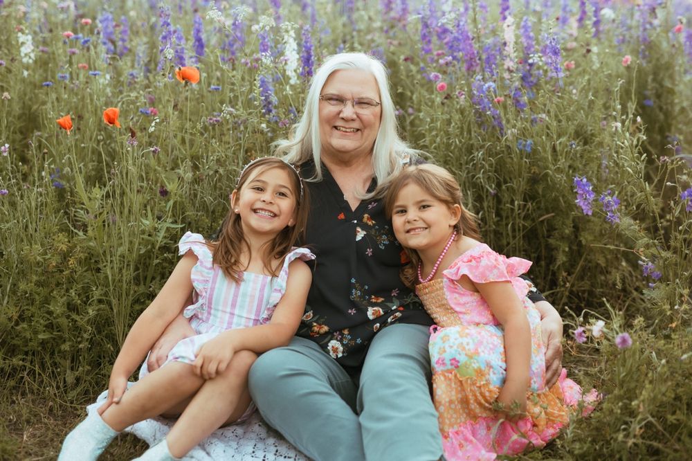 A family portrait session in a wildflower meadow with purple delphiniums and red poppies blooming in late summer.