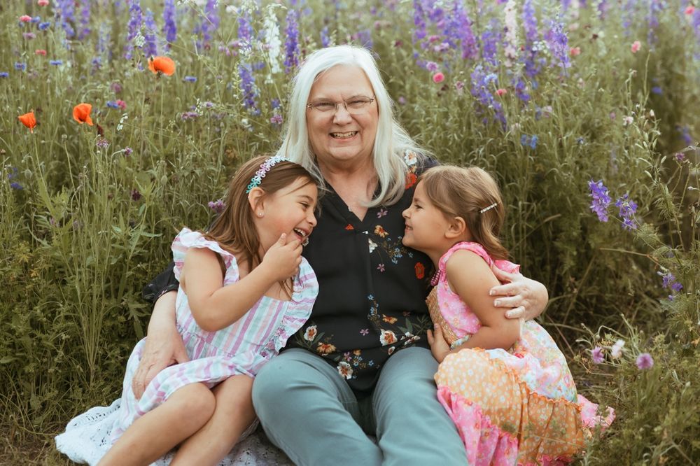 A heartwarming moment of laughter and hugs in a wildflower meadow with purple delphiniums and red poppies blooming.