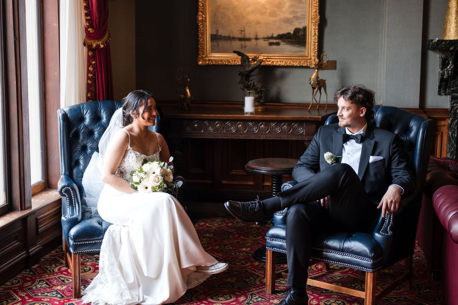 Formal wedding portrait of couple seated in vintage blue chairs in elegant room.
