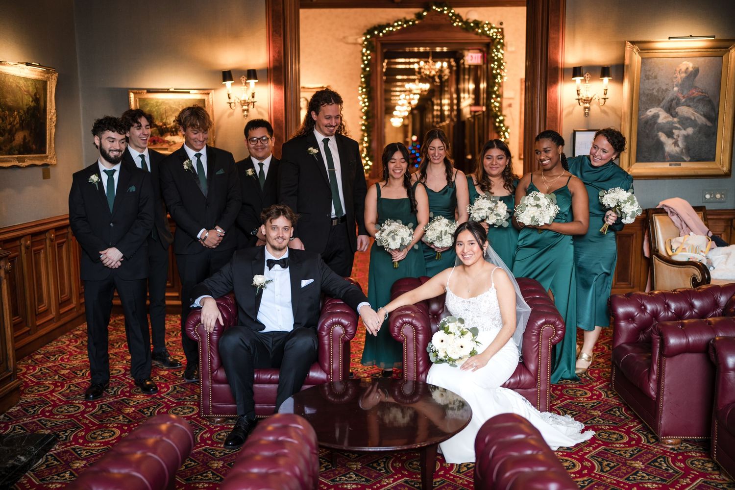 Large wedding party in formal attire posed together in elegant room with red furniture.