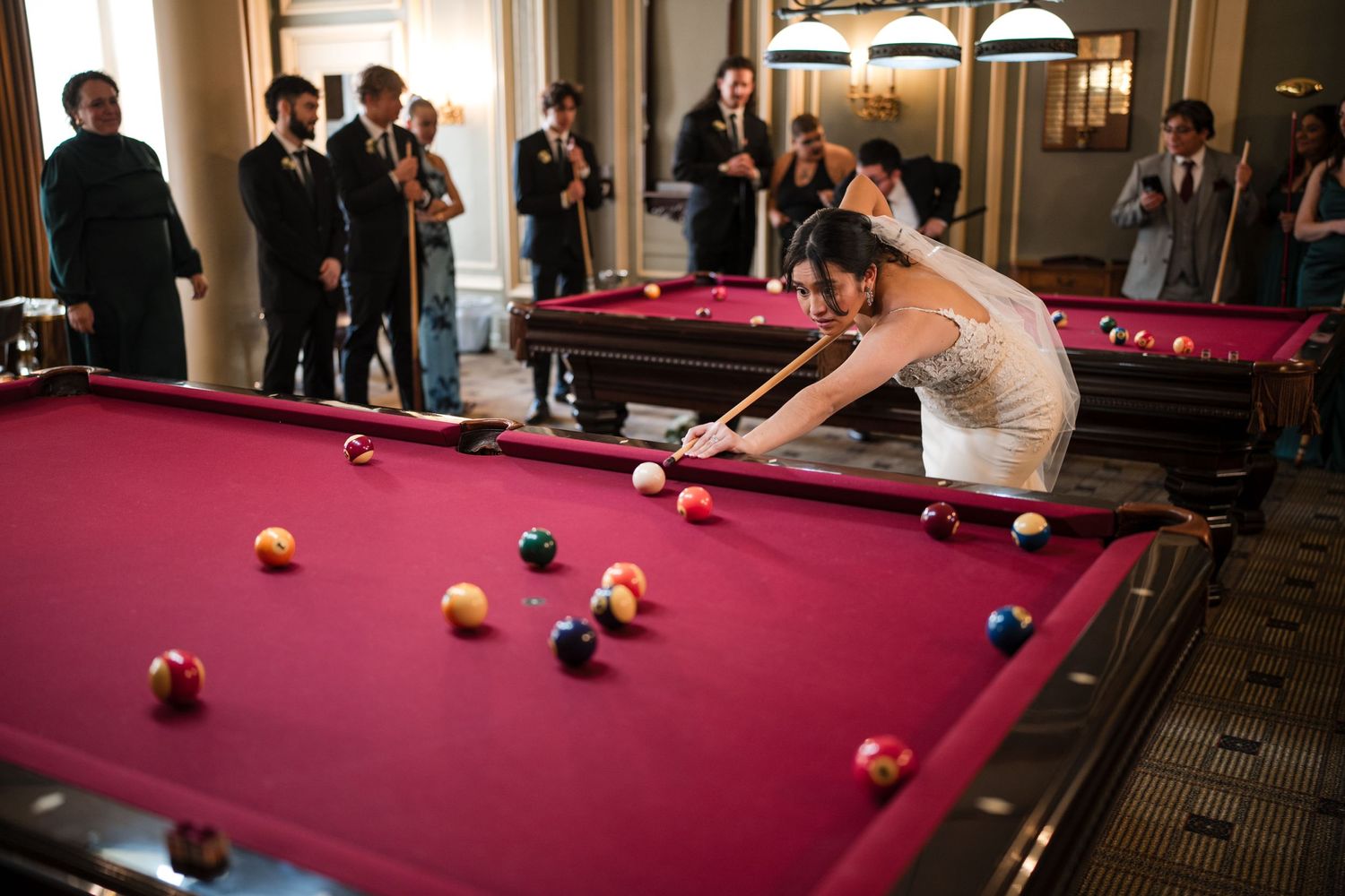 Wedding couple enjoying a game of pool in an elegant venue with guests watching.