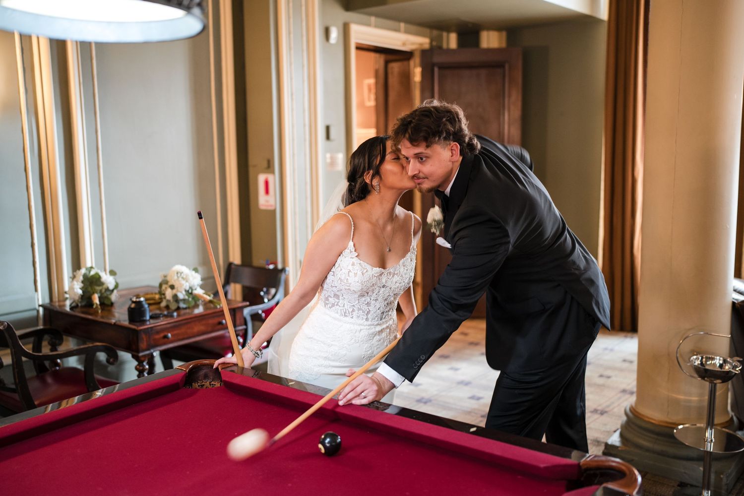 Newlyweds share a playful moment while playing billiards in their wedding attire.