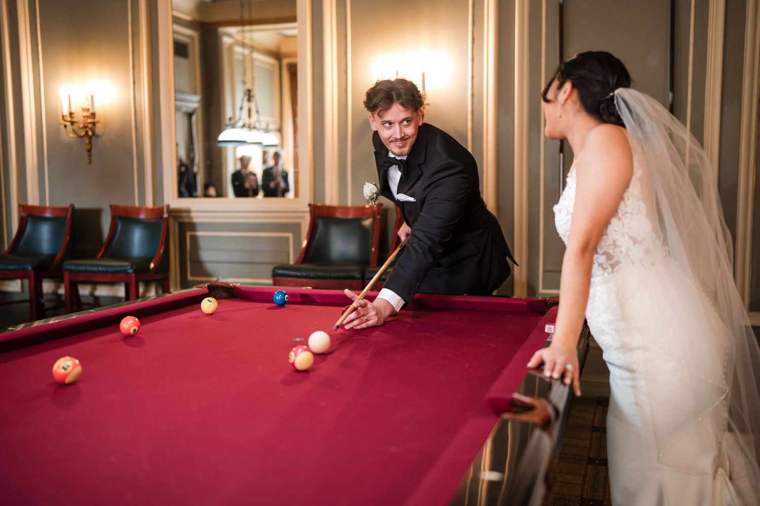 Couple in wedding attire playing pool together in an elegantly lit room.