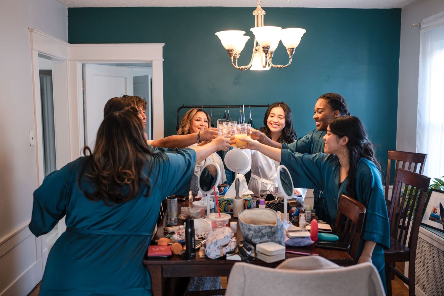 Group in teal robes toasting drinks around a table with celebration supplies.