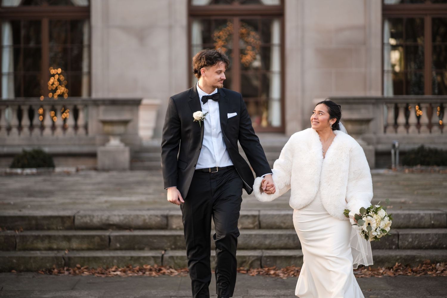Newlyweds walking down stone steps in formal wedding attire with autumn leaves in background.