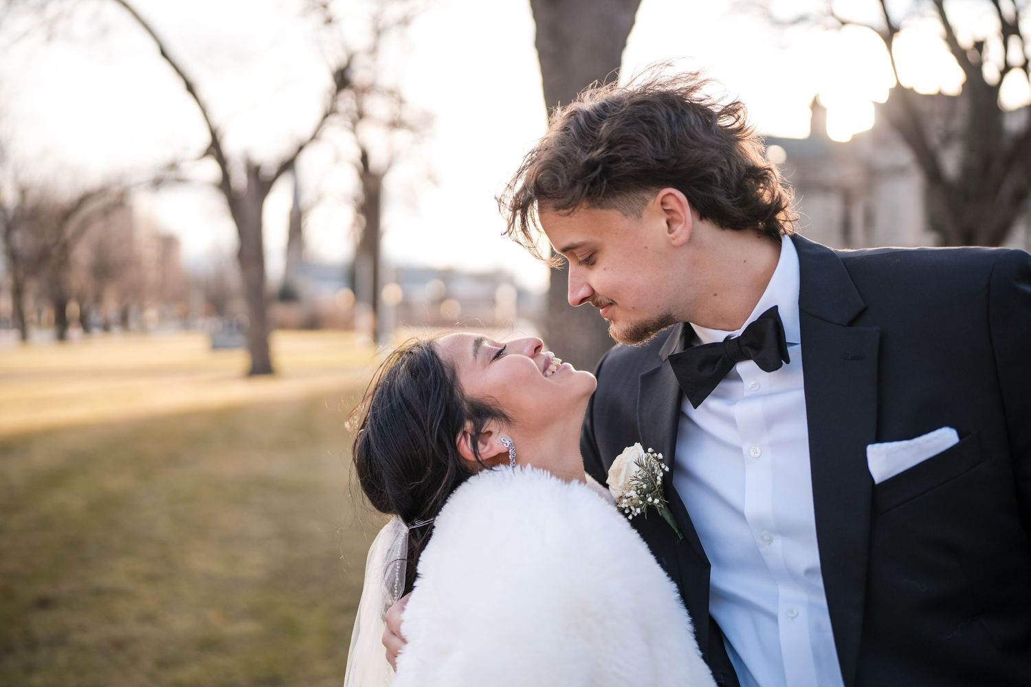 Romantic couple in winter wedding attire share a joyful moment on the grounds of a historic estate.