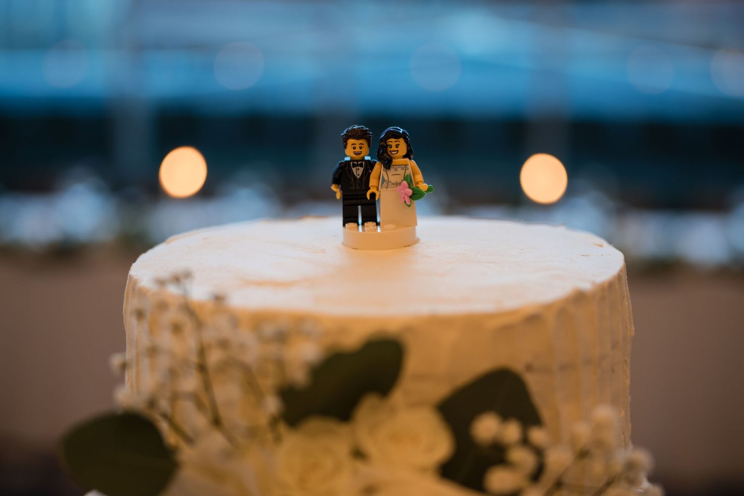 Close-up of wedding cake top with miniature bride and groom figures and delicate white frosting.