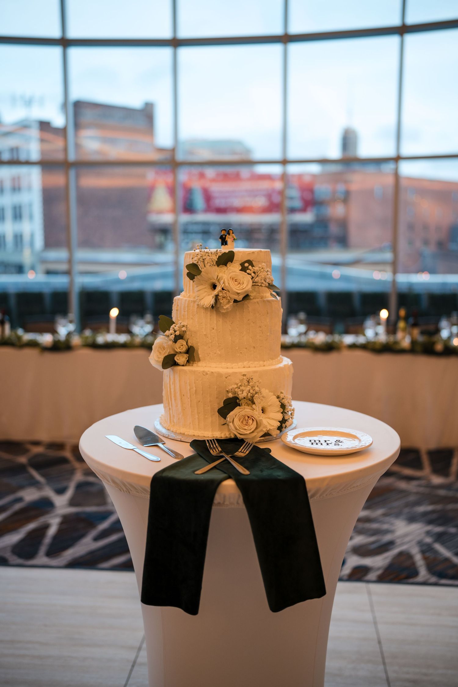 Elegant white wedding cake with floral decorations and black ribbon displayed on a pedestal table.