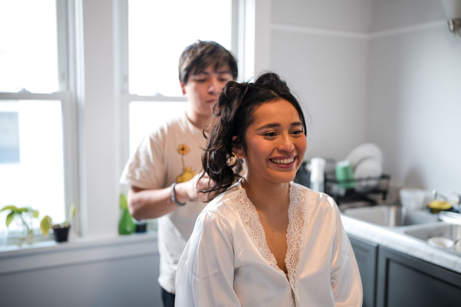 Two people share a joyful moment during wedding preparation in a bright kitchen setting.