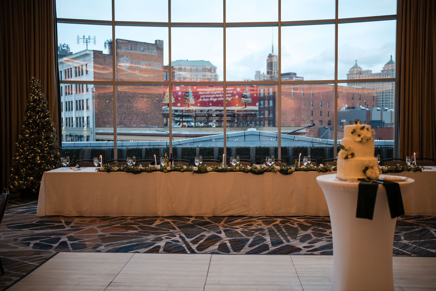 Wedding reception venue with city views through large windows and decorated tables.