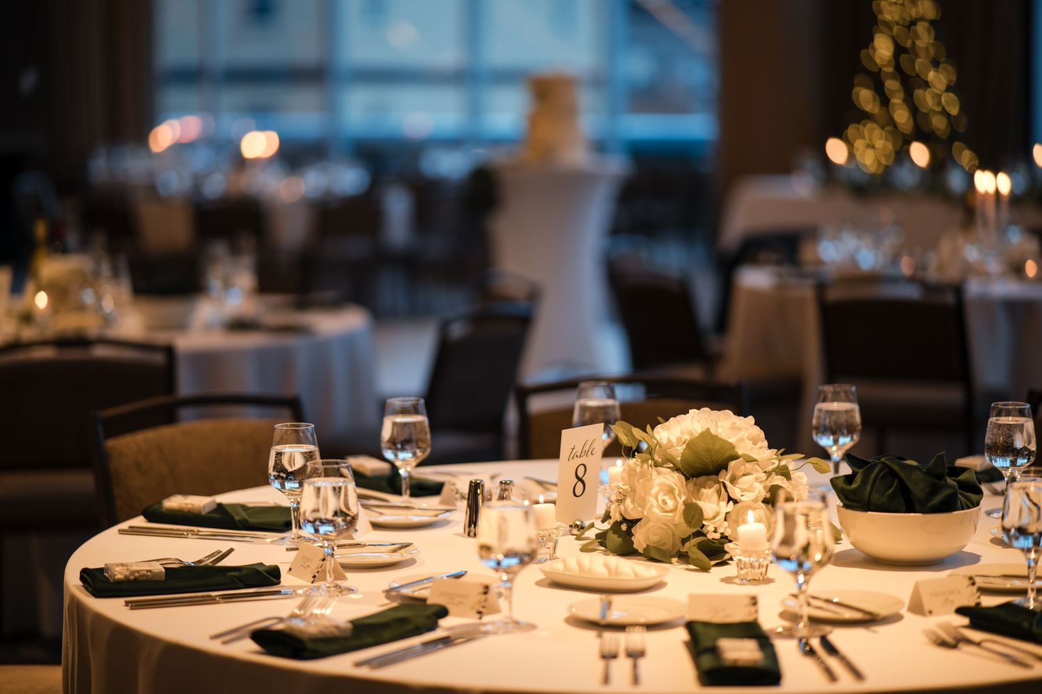 Formal round dining tables set for wedding reception with white floral centerpieces and wine glasses.