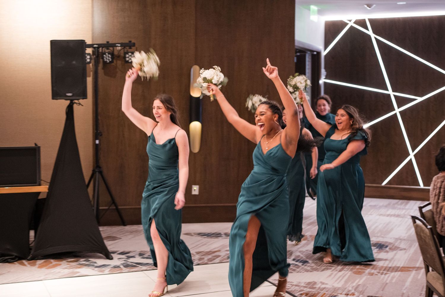 Wedding party in teal dresses celebrating on dance floor at reception.