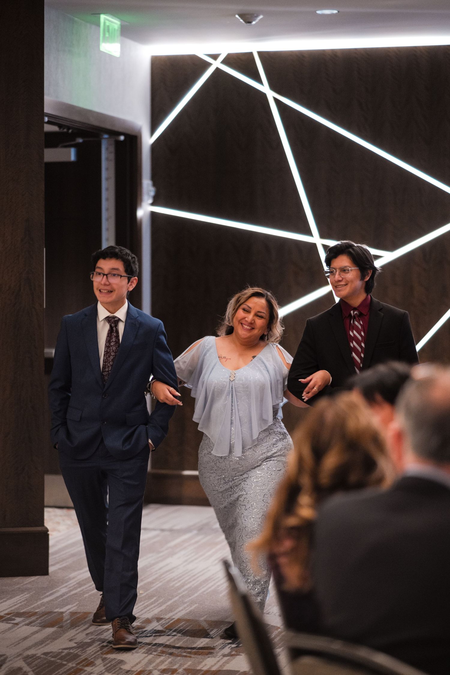 Wedding party members walk into a modern venue with geometric lighting design on the wall.