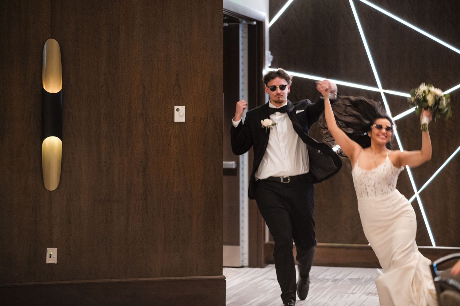 Couple makes a grand entrance at their wedding reception with geometric wall lighting.