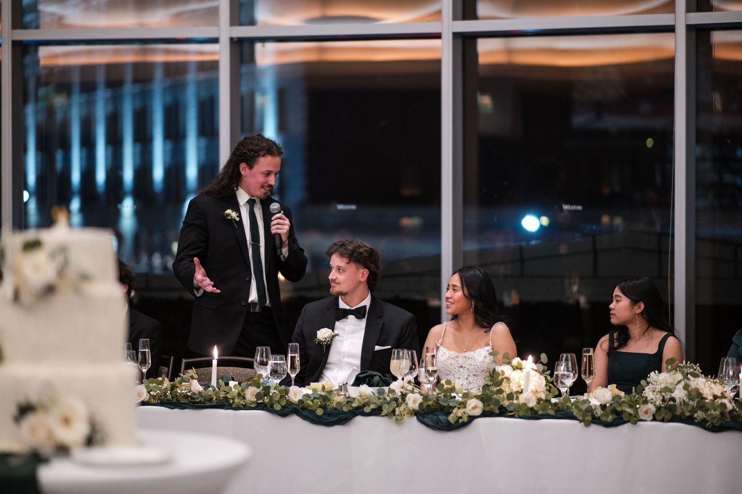 Wedding party seated at elegant head table with white floral decorations.