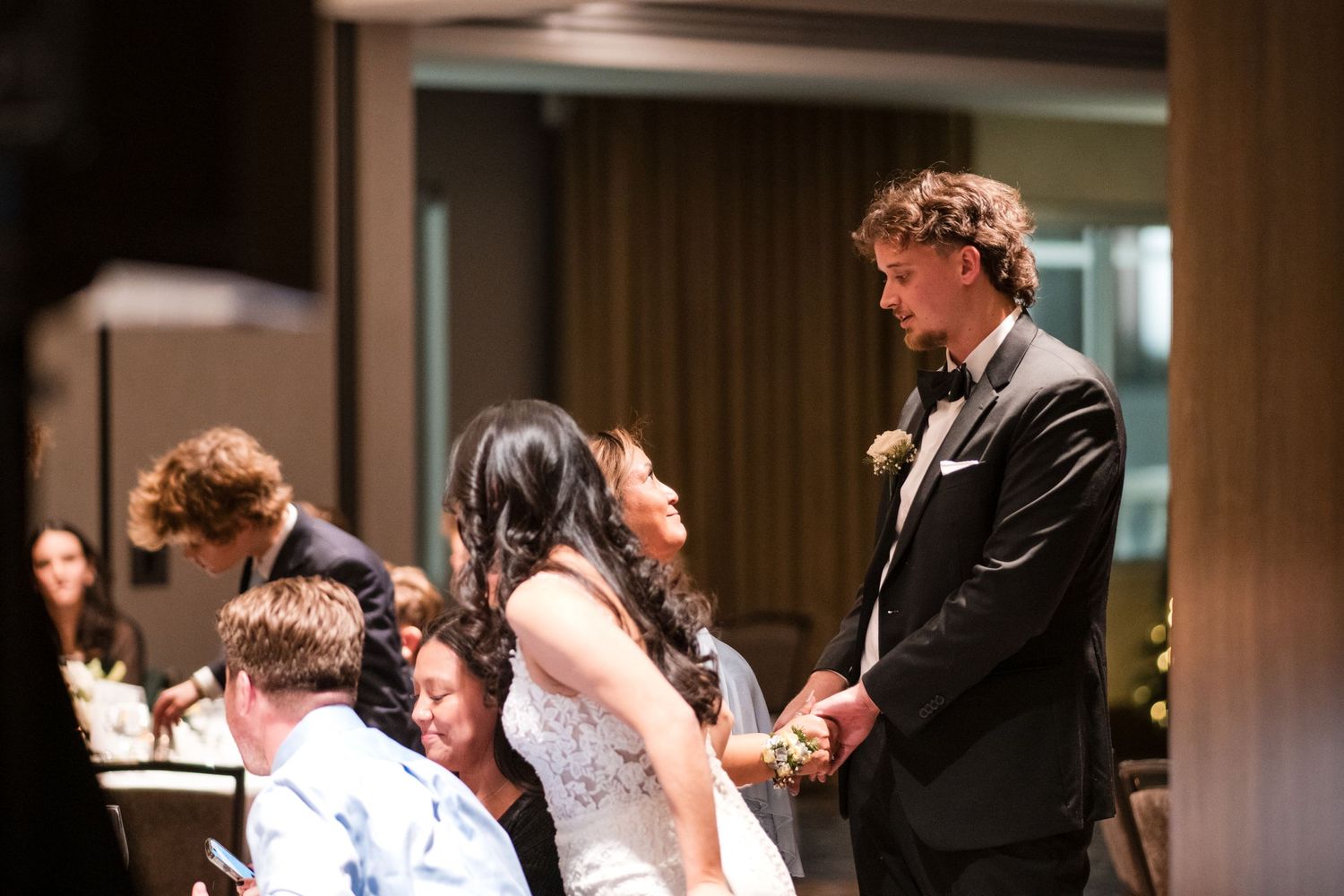 A joyful wedding celebration moment captured during an indoor reception with guests at decorated tables.