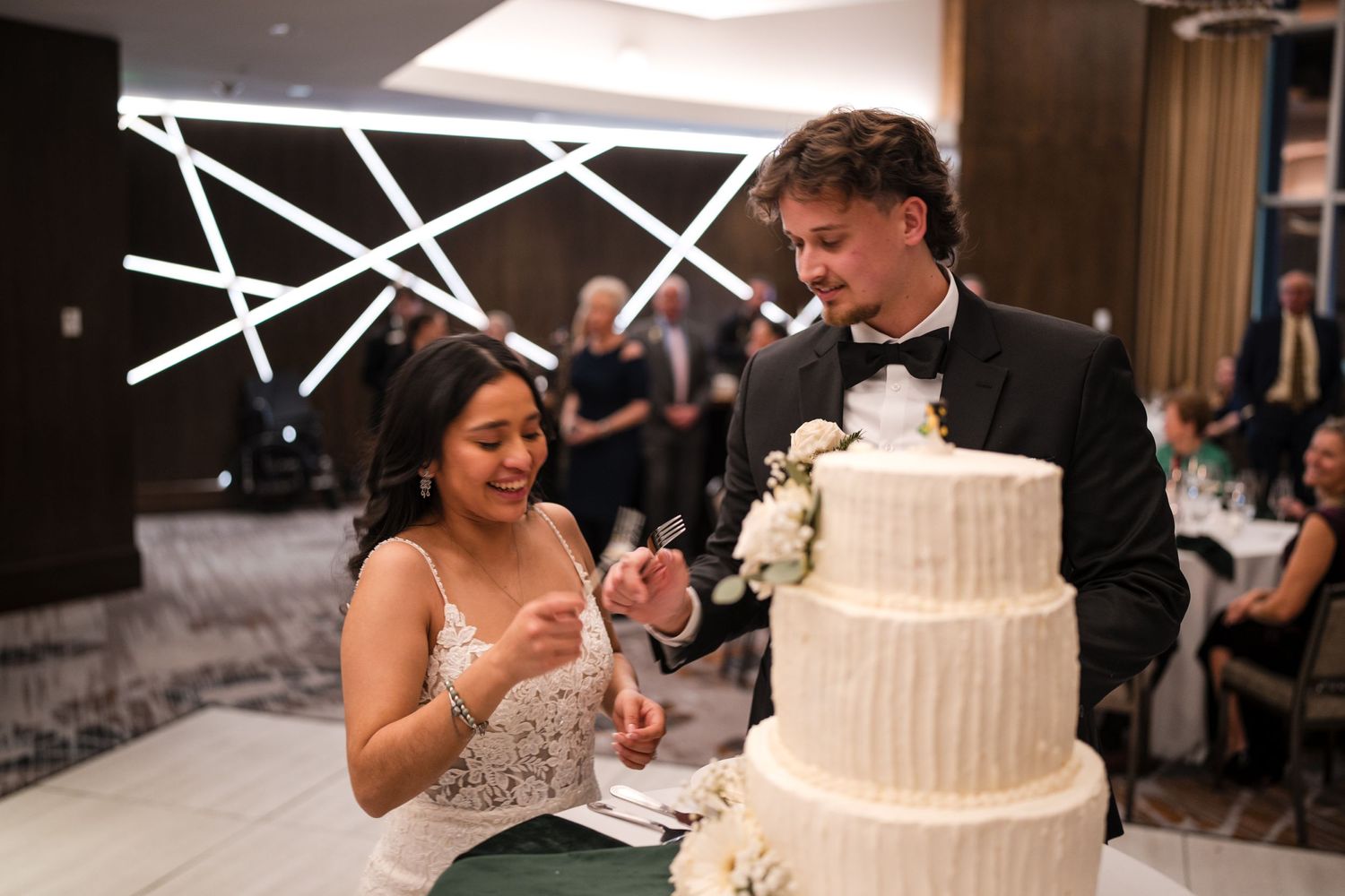Newlyweds share a sweet moment while cutting their elegant white tiered wedding cake.