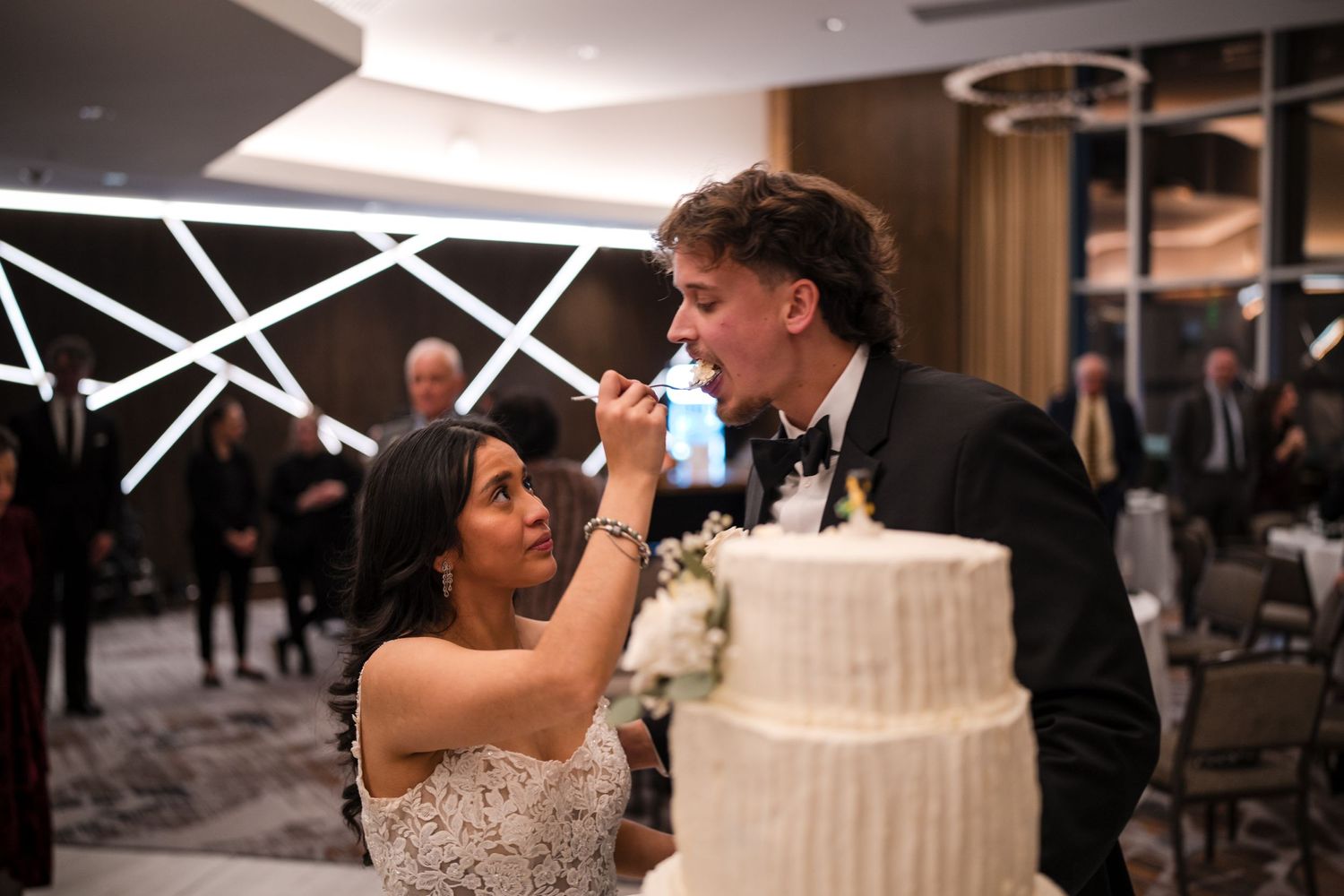 Playful moment as newlyweds feed each other wedding cake during their reception celebration.