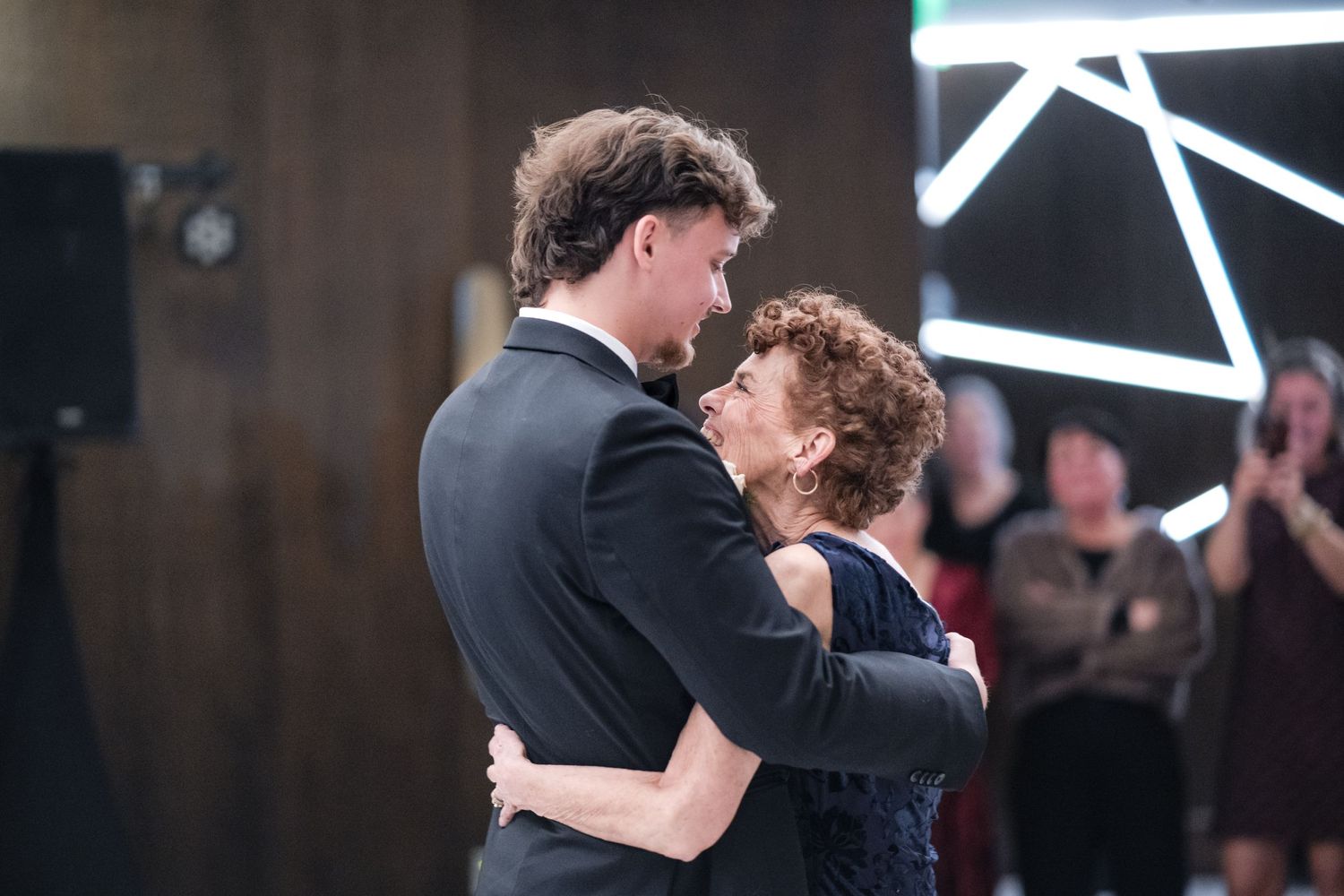 Tender embrace during a wedding dance with geometric lighting decor in the background.