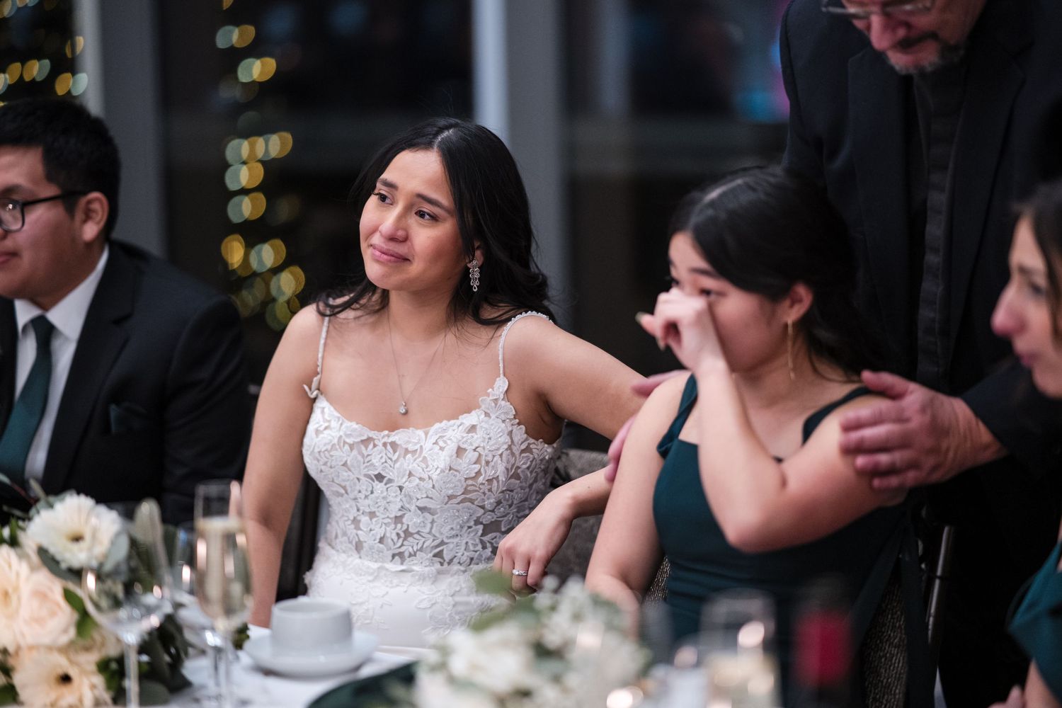 Emotional wedding reception moment with bride at decorated dinner table.