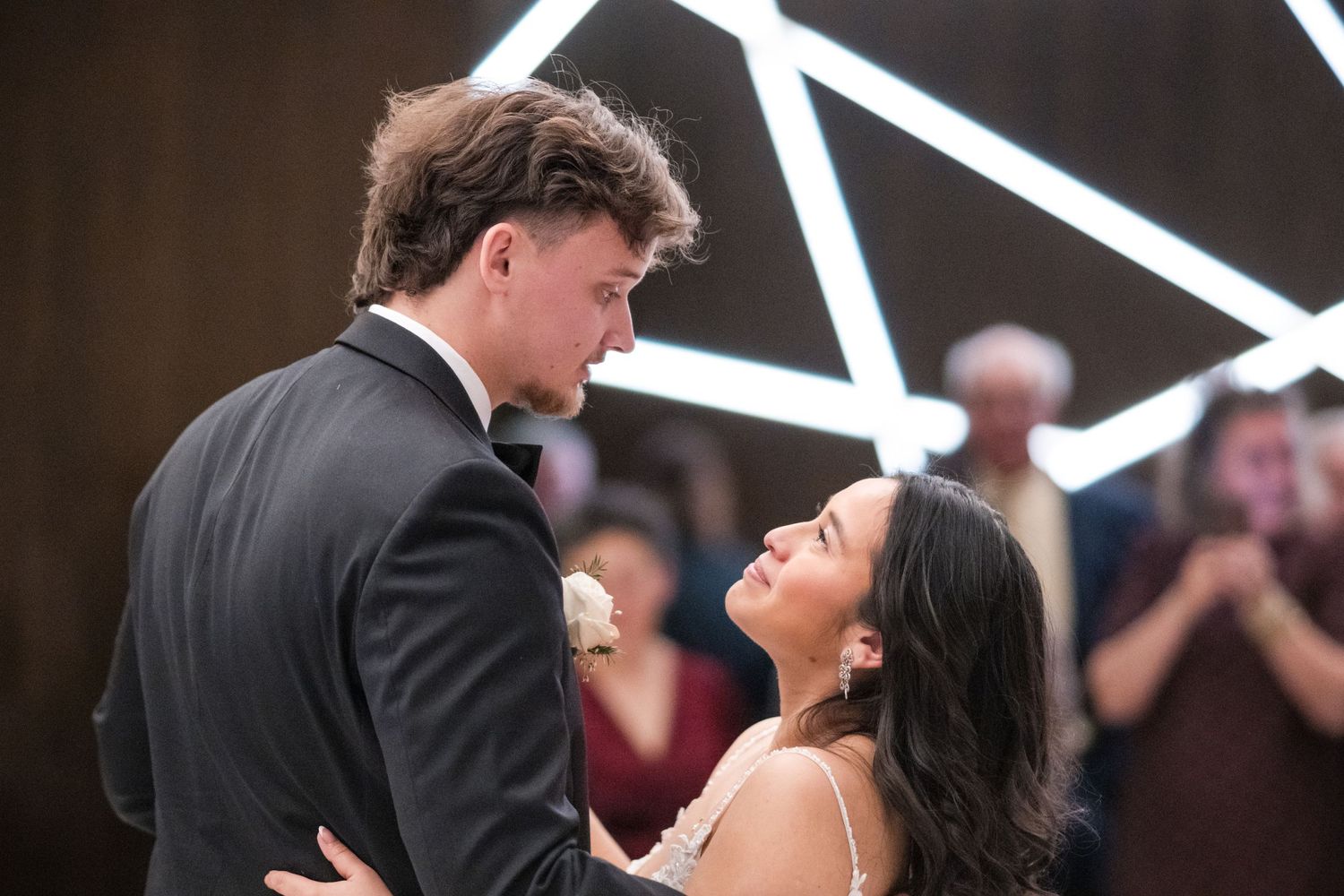 A romantic moment between newlyweds during their first dance with geometric lighting in background.