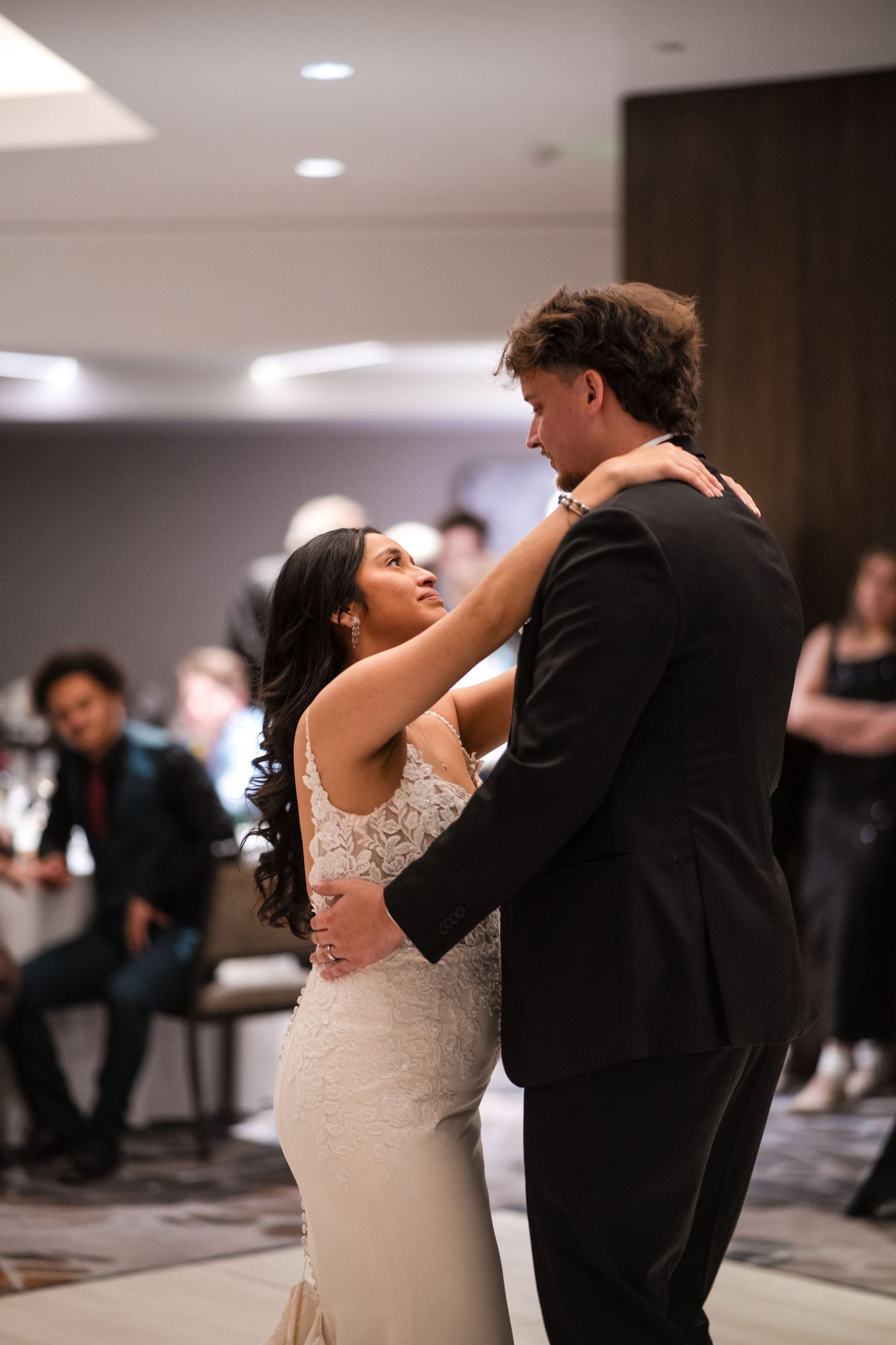 A couple shares their first dance at their wedding reception with the bride in a fitted lace gown and groom in black tuxedo.