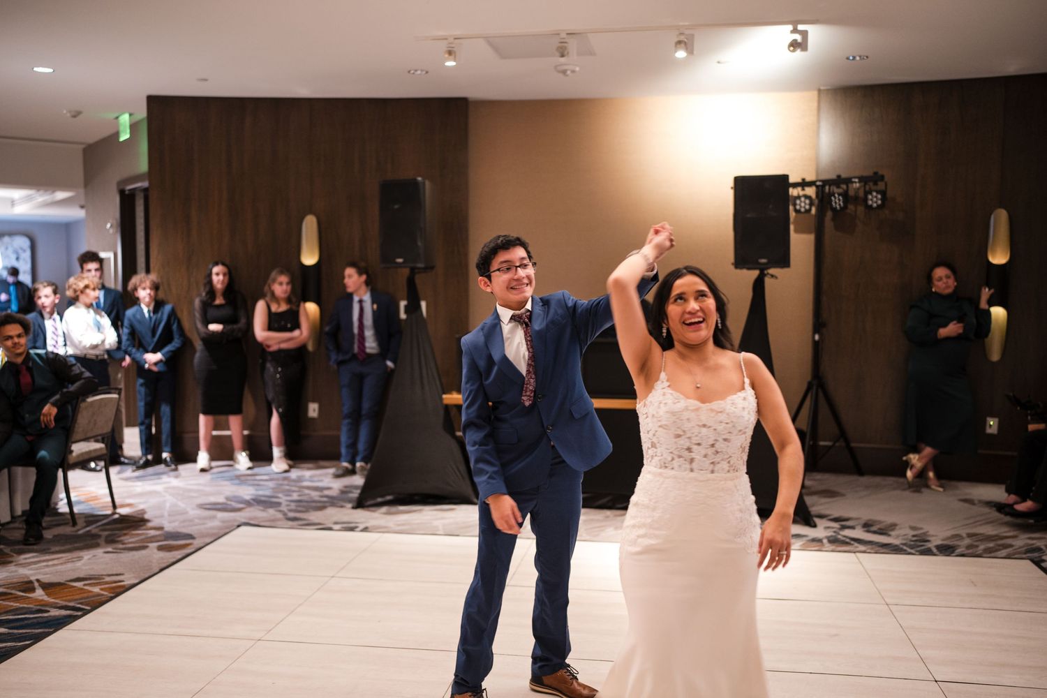 Bride in lace dress and groom in navy suit dance energetically at their wedding reception.