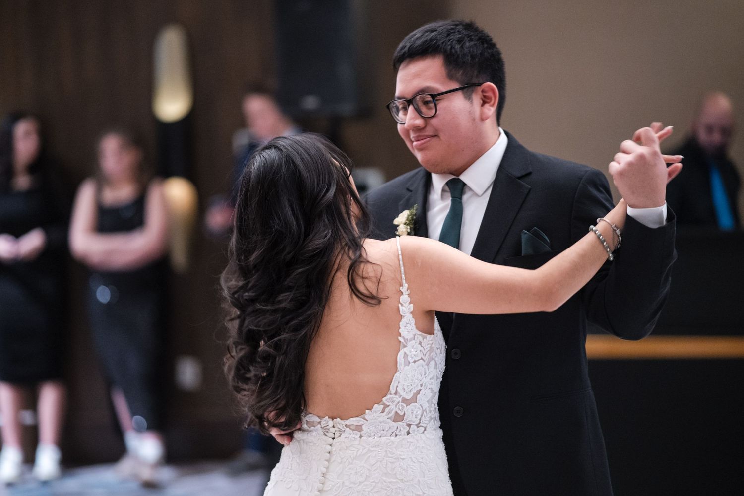 A couple performs their wedding dance in formal attire surrounded by guests.