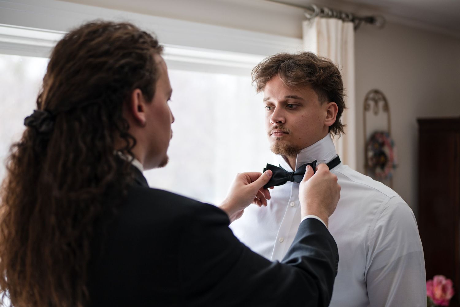 Someone helping adjust a black bowtie on a formal white dress shirt before a special event.