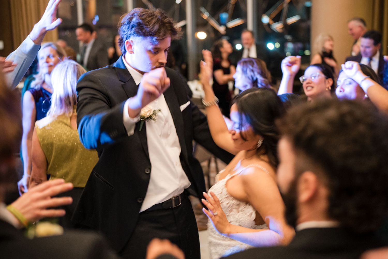 Energetic dancing and celebration at a wedding reception with blue lighting effects.
