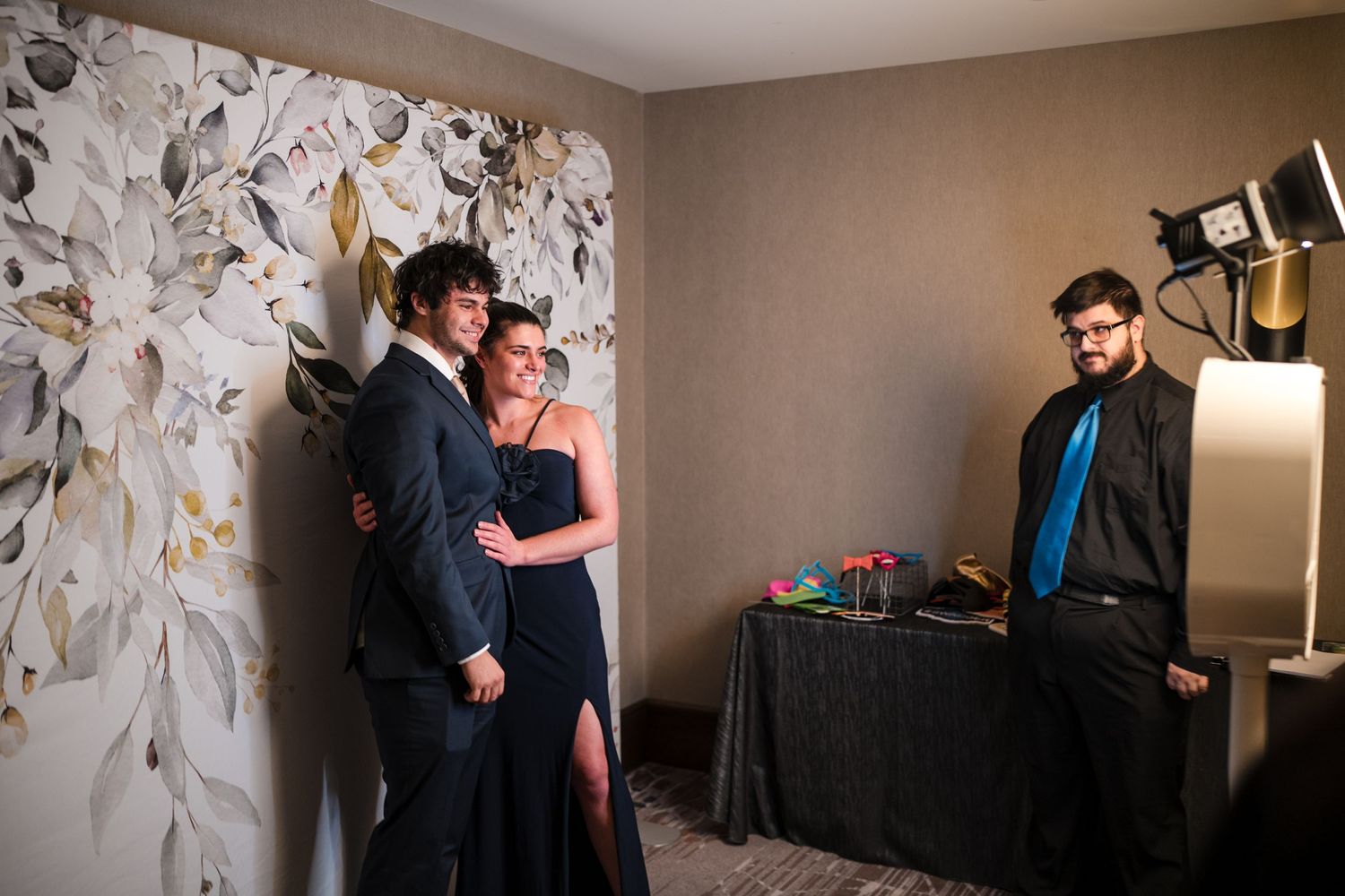 Wedding party poses for photos against a floral backdrop in an elegant venue.