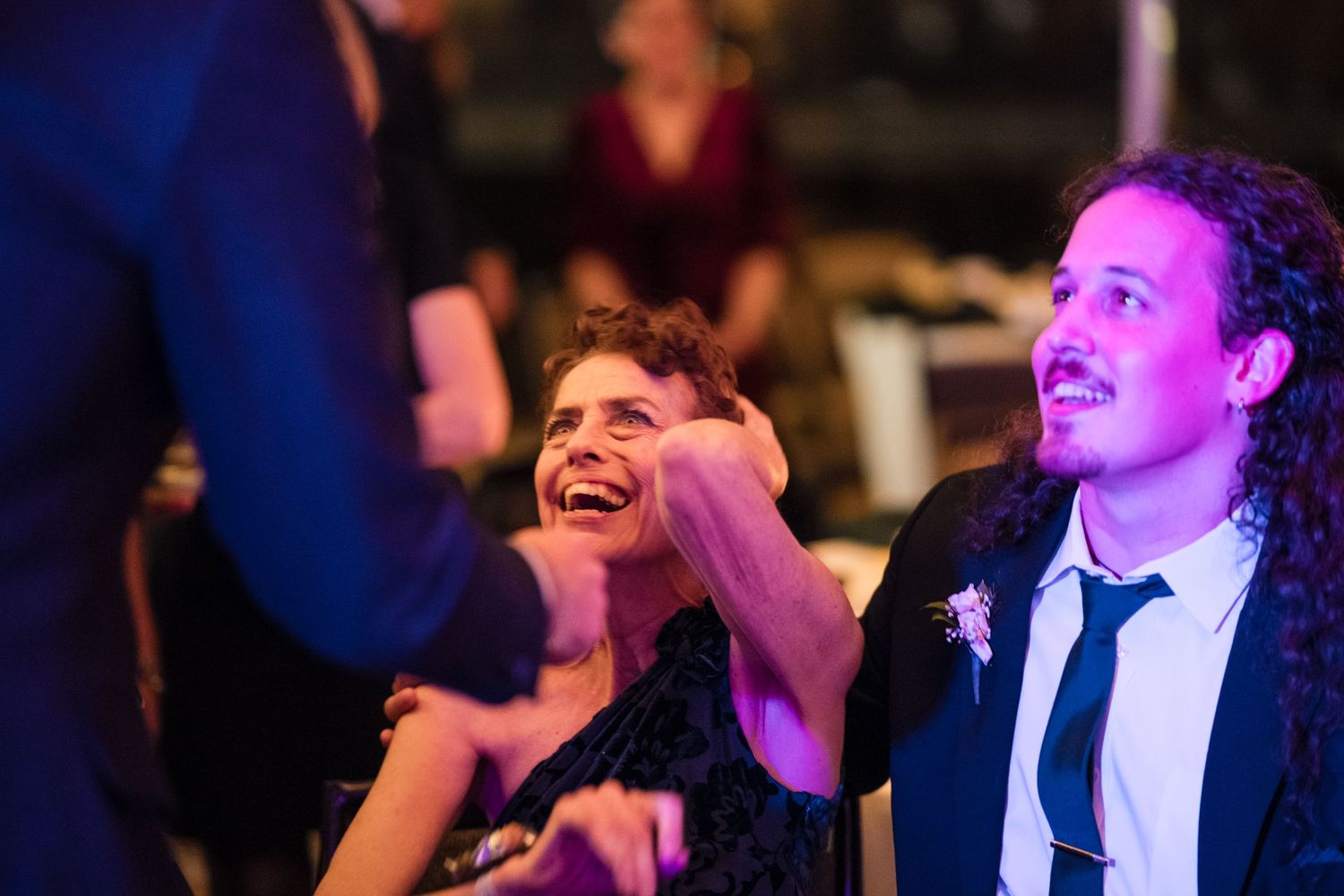 Wedding celebration with joyful guests laughing under ambient lighting.