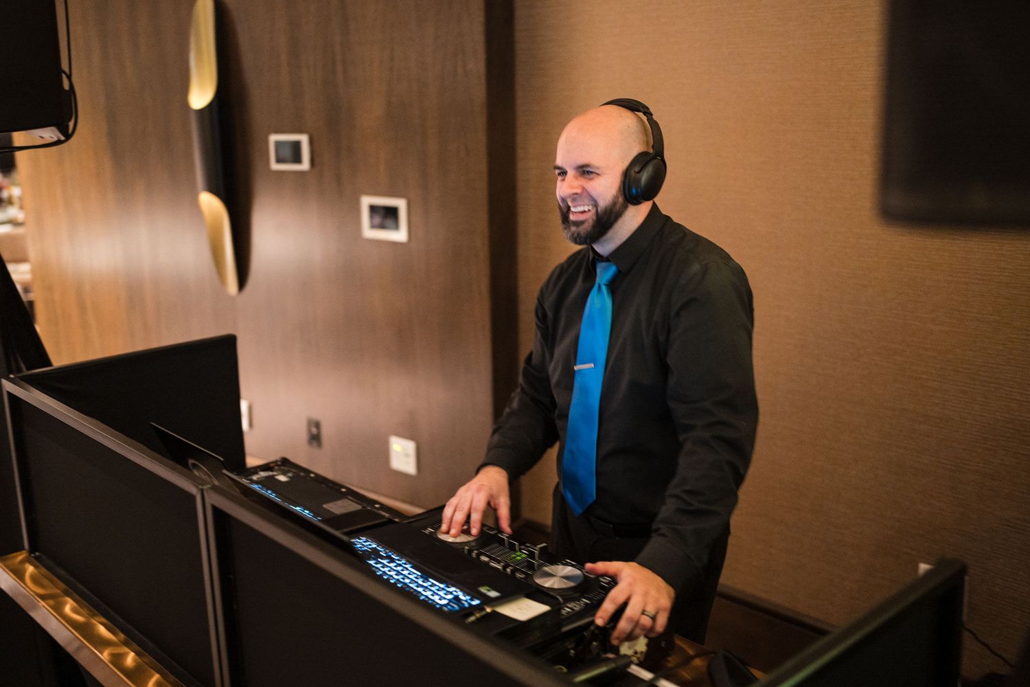 DJ in black jacket and blue tie performs with keyboard at indoor event.