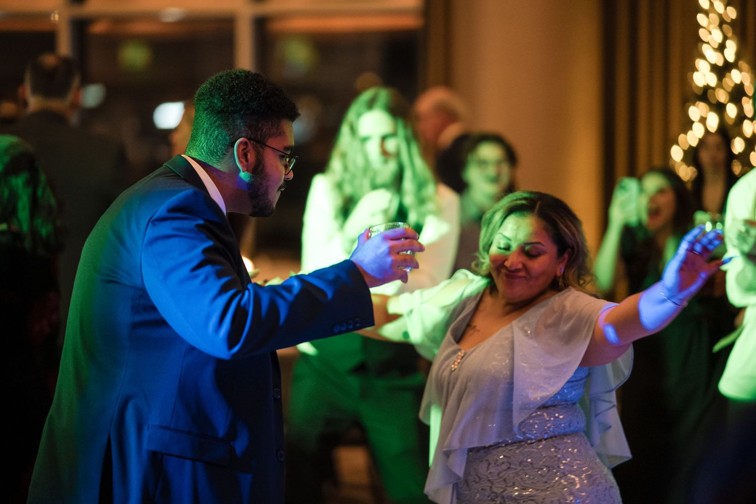 Guests dancing under green lighting at evening reception party.