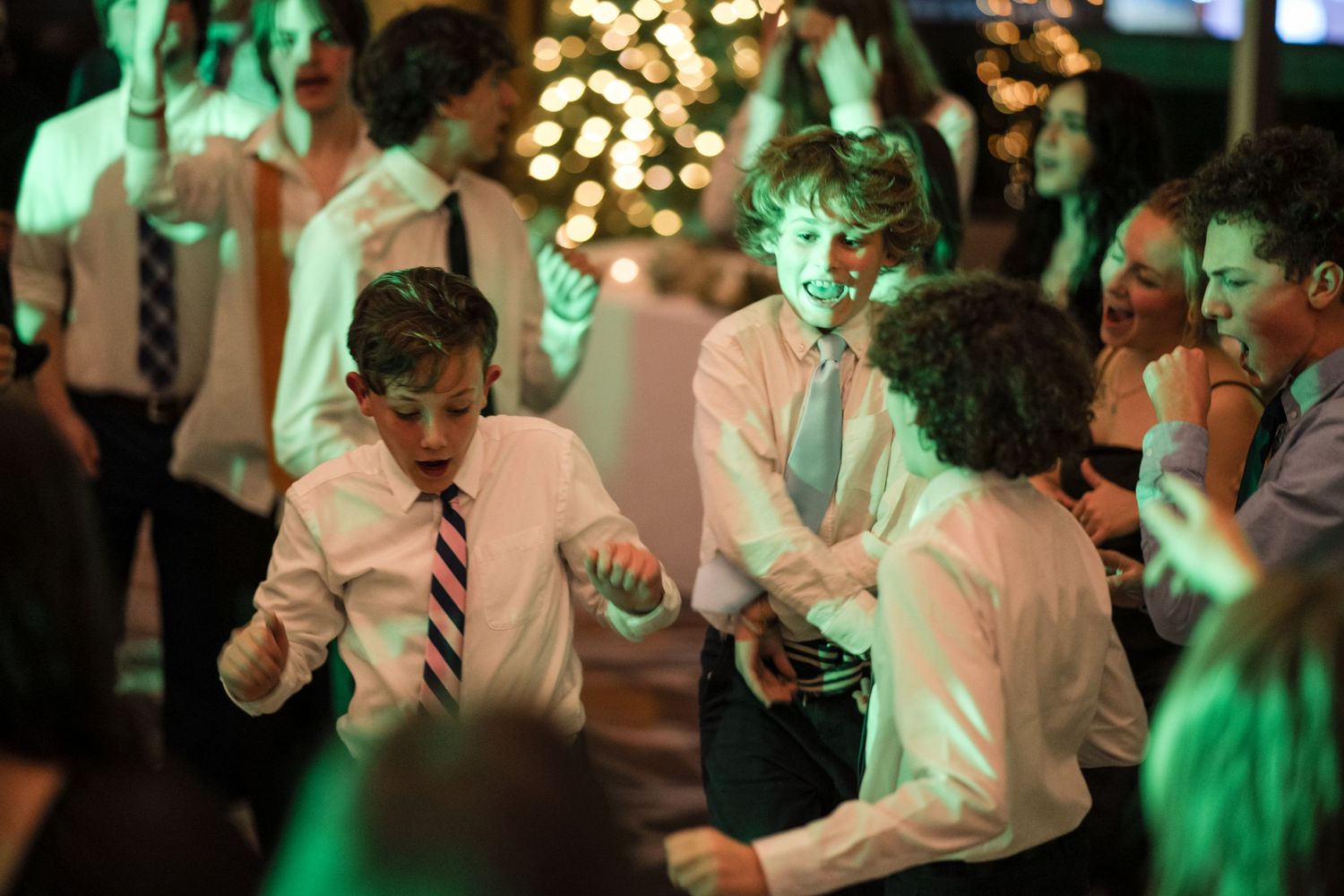 Young guests dancing energetically under green ambient lighting at party.