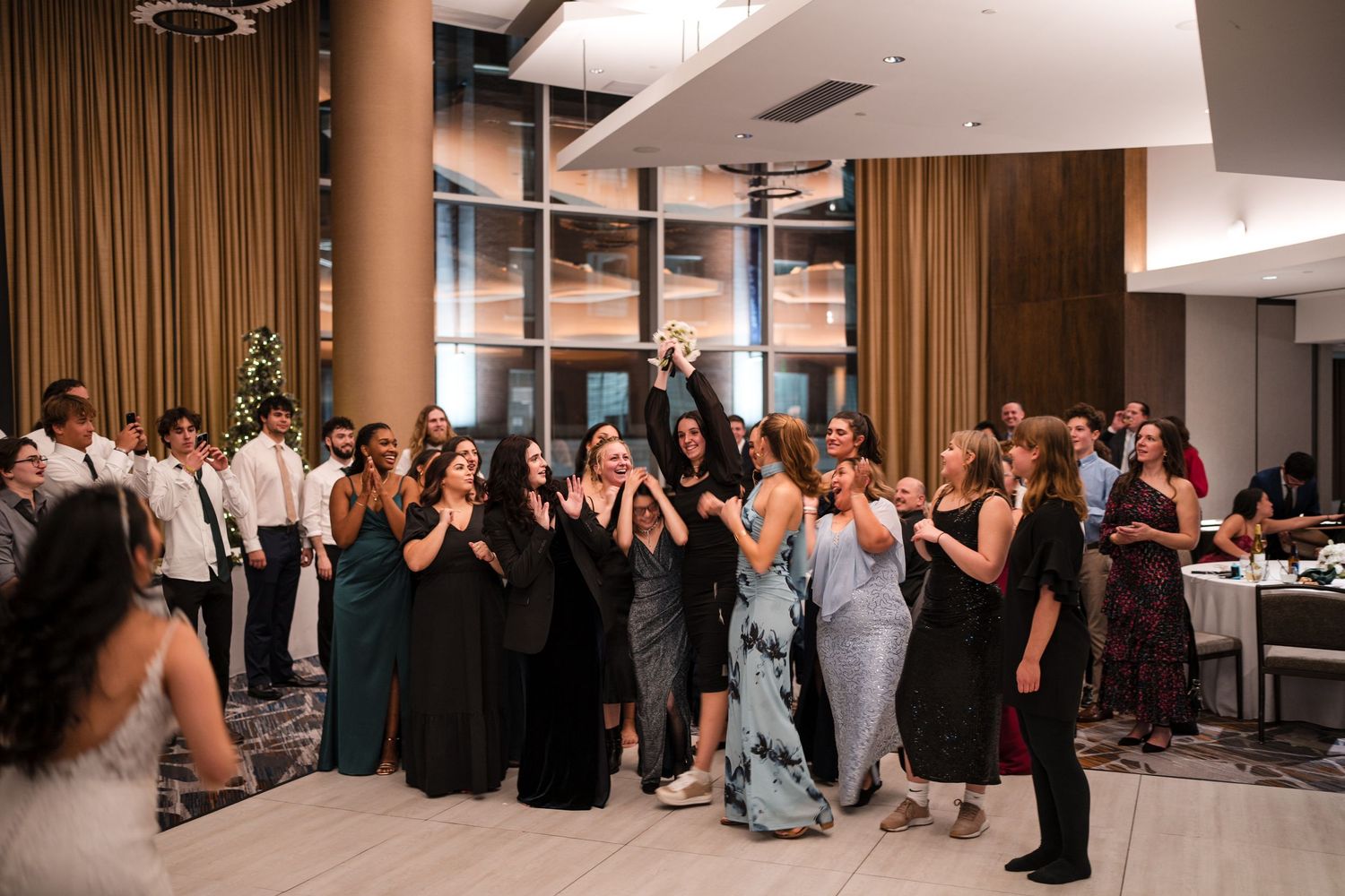 Guests in formal wear join together for a group dance moment at an elegant indoor wedding reception.