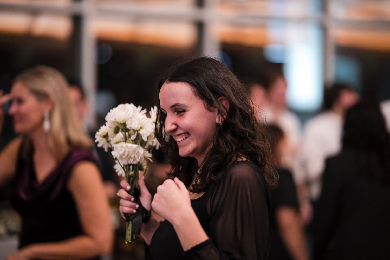 Guest smelling a white floral bouquet during an evening wedding celebration.